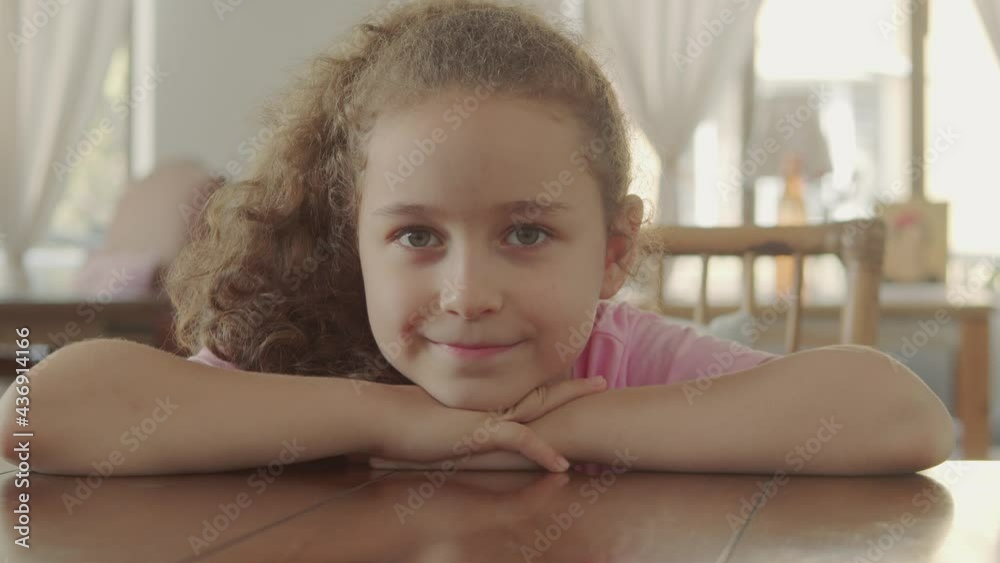 Portrait of a happy little girl, smiling child, looking at the camera, sitting at the table in a cafe, cute baby child with a beautiful face, kid sitting at the table at home. Happy childhood concept. Portrait of a happy little girl, smiling child, looking at the camera, sitting at the table in a cafe, cute baby child with a beautiful face, kid sitting at the table at home. Happy childhood concept.