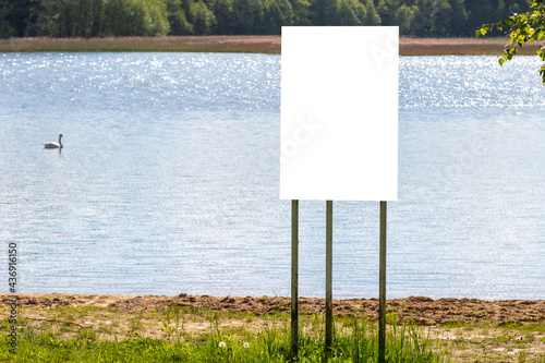 Fototapeta Naklejka Na Ścianę i Meble -  A white banner stands on the lake shore with a mockup. A swan is floating in the background
