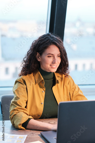 Young smiling woman sitting at the table and working on computer at office