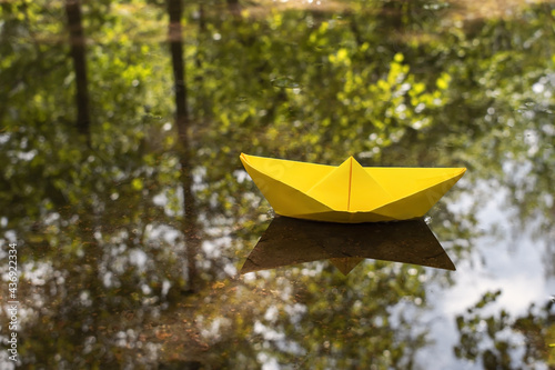 Yellow paper boat in a puddle with the reflection of trees