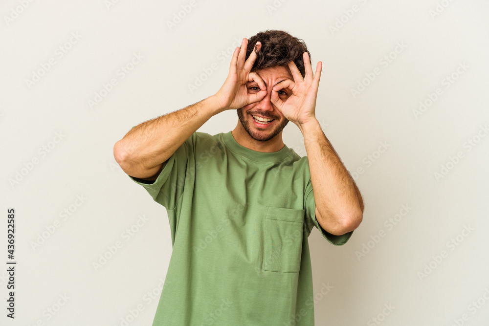 Young caucasian man isolated on white background showing okay sign over eyes Young caucasian man isolated on white background showing okay sign over eyes