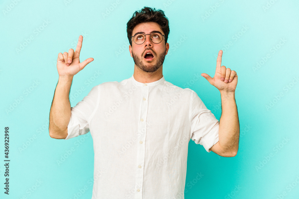 Young caucasian man isolated on blue background pointing upside with opened mouth. Young caucasian man isolated on blue background pointing upside with opened mouth.