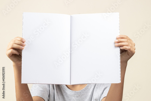 Kid hands holding open notebook with blank white pages in front of him