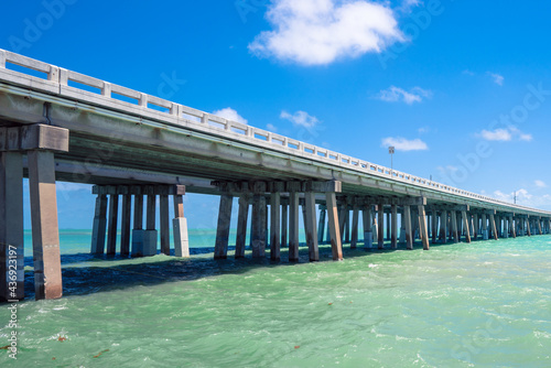 Highway concrete bridge across turquoise ocean water in Florida. Green water, concrete pilots, blue sky with soft clouds and speed limit sign. Driving across the sea in tropical paradise © Petr