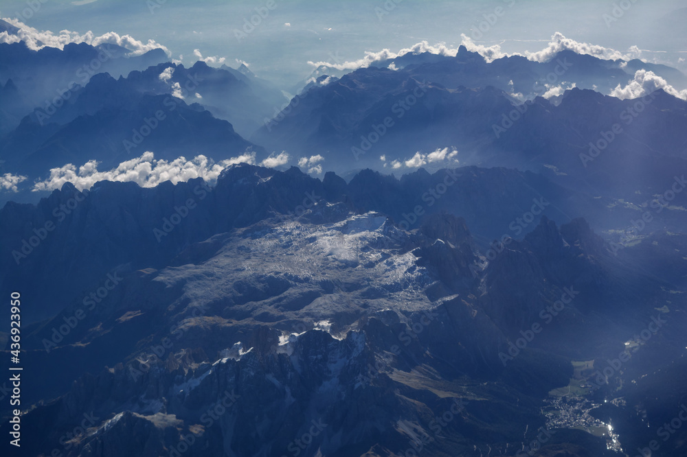 Aerial view of snowy mountains and clouds, opposite the sunlight