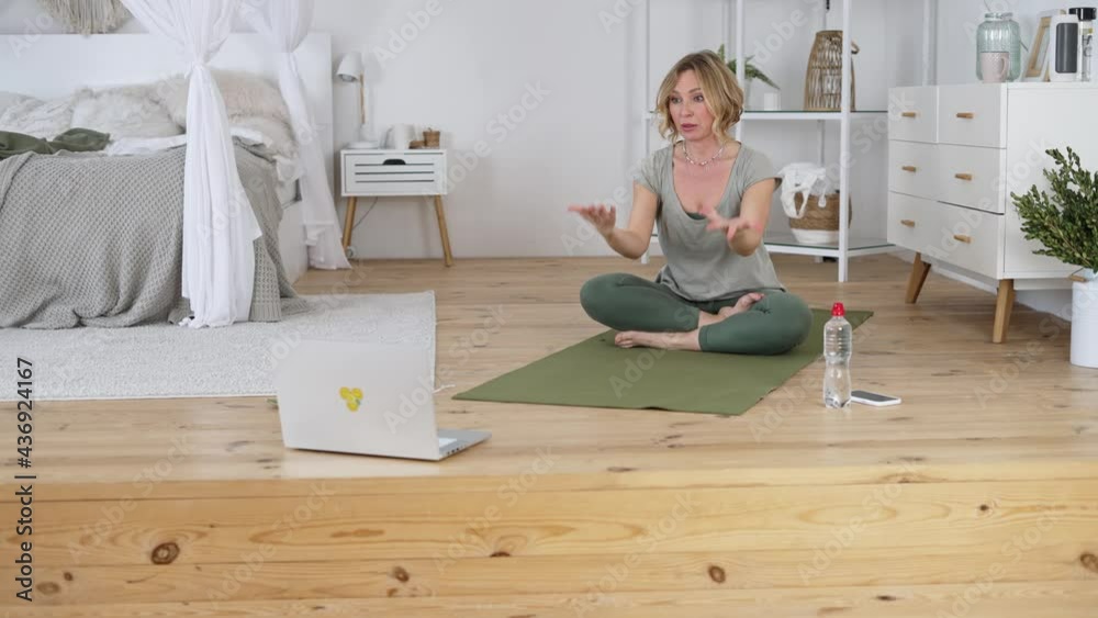 Professional yoga instructor looking at laptop camera during online lesson, sitting on mat and showing students exercise and helpful breathing technique. Healthy lifestyle and remote sports training Professional yoga instructor looking at laptop camera during online lesson, sitting on mat and showing students exercise and helpful breathing technique. Healthy lifestyle and remote sports training