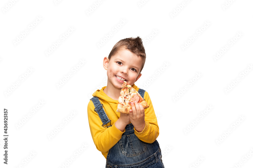 Little cute toddler boy in a yellow sweater and denim overalls holds a slice of pizza near his mouth and smiles beautifully. Little cute toddler boy in a yellow sweater and denim overalls holds a slice of pizza near his mouth and smiles beautifully.