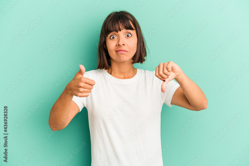 Young mixed race woman isolated on blue background keeps hands under chin, is looking happily aside. Young mixed race woman isolated on blue background keeps hands under chin, is looking happily aside.