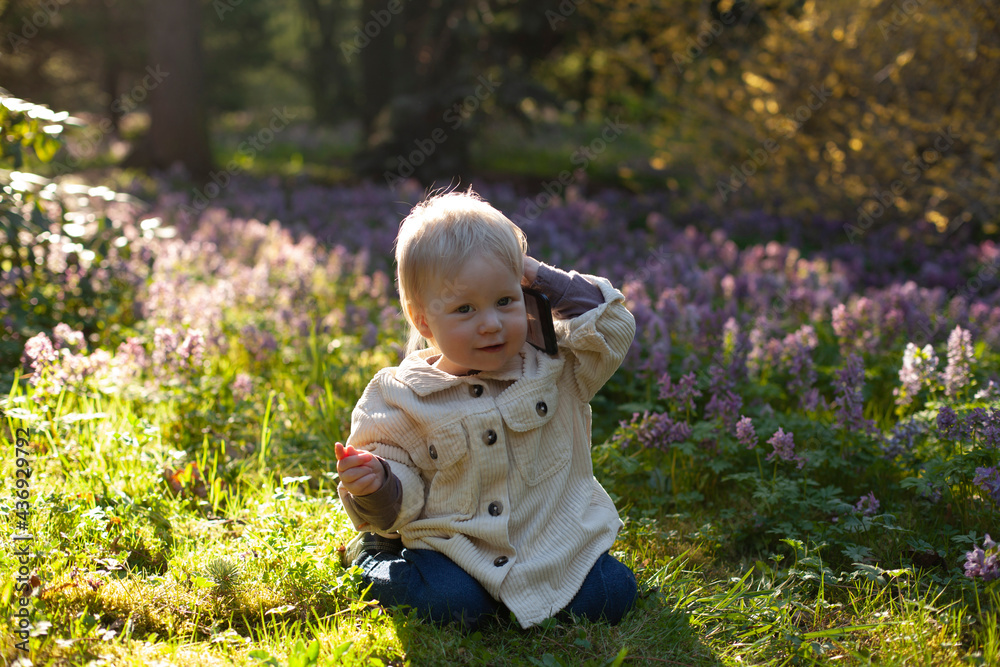 Cute baby boy sits on a beautiful field and talking on phone. Kid's playing. Cute baby boy sits on a beautiful field and talking on phone. Kid's playing.