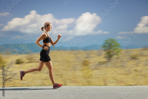 Profile shot of a fit young woman jogging on an open road
