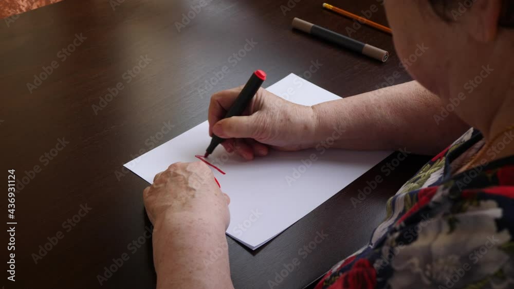 An elderly artist woman writes on a piece of paper NFT Token (Non-Fungible Token) and dreams of selling her works at an online auction and earning Ethereum cryptocurrency. 