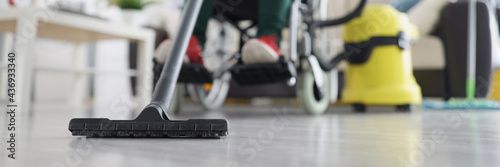 Fototapeta Naklejka Na Ścianę i Meble -  Woman in wheelchair vacuuming floor at home closeup