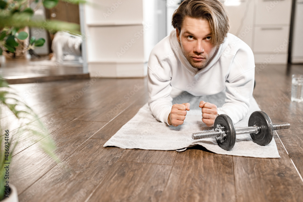 Concentrated male is working out at home in the morning, doing plank pose. Athletic caucasian man is training, exercising to keep good shape, motivates to healthy lifestyle, wellness concept Concentrated male is working out at home in the morning, doing plank pose. Athletic caucasian man is training, exercising to keep good shape, motivates to healthy lifestyle, wellness concept