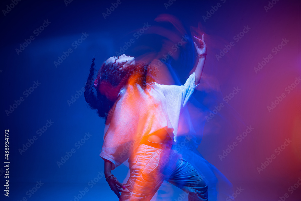 Cool dancing young mixed race girl in colorful neon studio light. Long exposure. Contemporary hip hop dance, rap rhythm - obrazy, fototapety, plakaty 