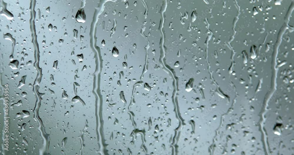 Close-up of raindrops dripping down a glass window with blurry background Close-up of raindrops dripping down a glass window with blurry background