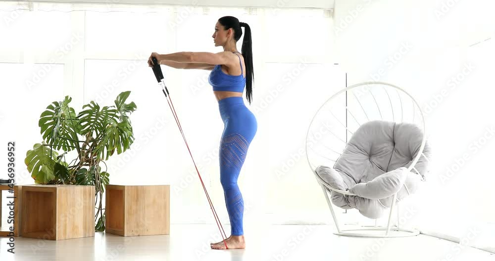 A sporty woman is doing exercises on quarantine. The woman is getting fit and using a fitness band to strengthen her muscles.