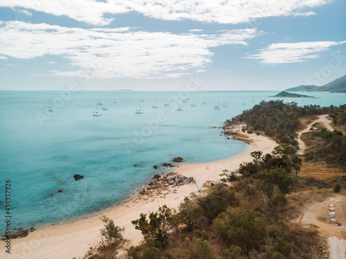 Aerial view of a beach at Hideaway Bay with a couple walking on the beach and catamarans anchored along the coast, Queensland, Australia.