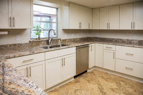 A Modern U-Shaped Kitchen with White Cabinets, Granite Countertops and a Touchless Faucet with Double Bowl Stainless Steel Sink in Front of a Window. photo