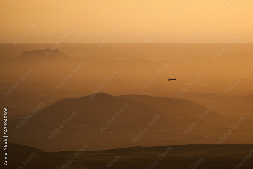 Aerial view of a helicopter flying low in the mist with a beautiful landscape in background at sunset, Grindavík, Southern Peninsula, Iceland. Aerial view of a helicopter flying low in the mist with a beautiful landscape in background at sunset, Grindavík, Southern Peninsula, Iceland.