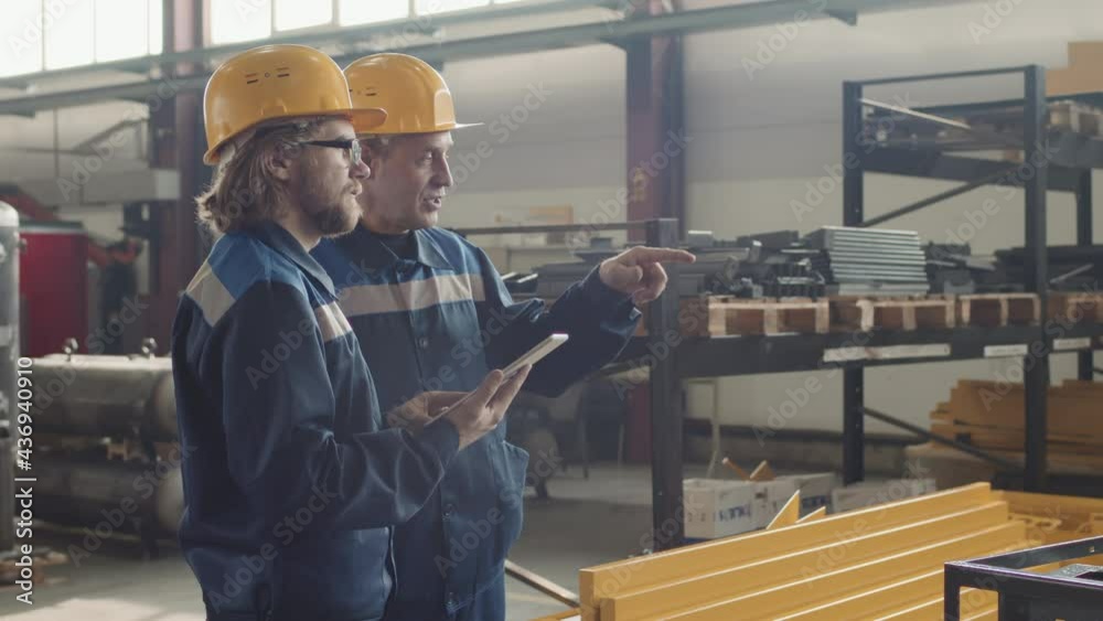Side-view medium slowmo of adult male plant supervisor gesticulating while talking to workman with tablet looking straight ahead Side-view medium slowmo of adult male plant supervisor gesticulating while talking to workman with tablet looking straight ahead