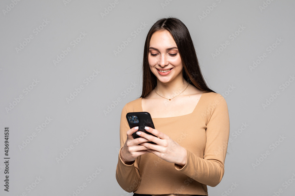 Portrait of a happy young woman using smartphone isolated on a gray background