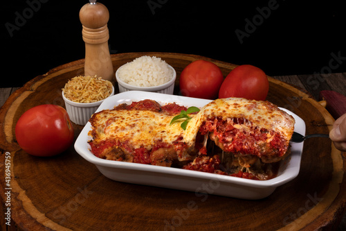 Steak Parmegiana or Parmegian Filet, made with breaded steak, tomato sauce, cheese au gratin. Accompanied by white rice and potato straw. Hand picking up food with spatula to serve.