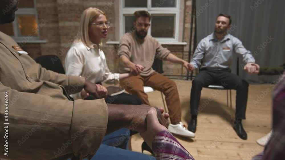 Diverse group of people sitting together in circle holding hands having support meeting with female specialist