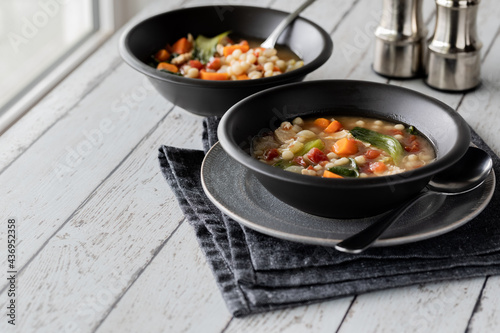 Two bowls of chicken and vegetable couscous soup against a sunny window.