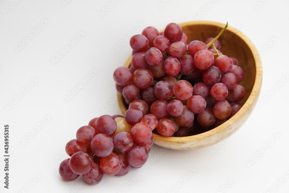 Obraz premium Fresh and ripe red grapes in a wooden bowl, isolated in white background. Bunch of raw and juicy grapevines