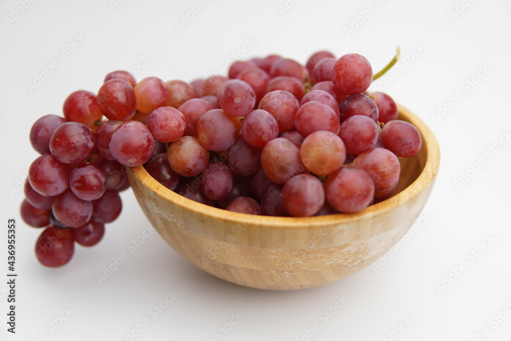 Fresh and ripe red grapes in a wooden bowl, isolated in white background. Bunch of raw and juicy grapevines Fresh and ripe red grapes in a wooden bowl, isolated in white background. Bunch of raw and juicy grapevines