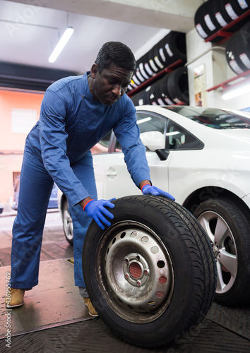 Afro american auto mechanic in uniform holds wheel at tire service