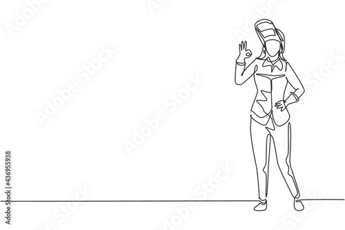 Single one line drawing female welder stands with gesture okay and face shield is removed ready to work in his iron workshop. Success business. Continuous line draw design graphic vector illustration