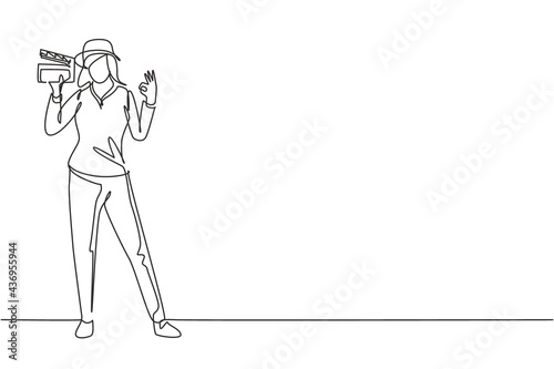 Single continuous line drawing female film director stands with gesture okay holding clapperboard and prepare camera crew for shooting at studio. One line draw graphic design vector illustration