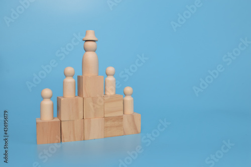 Wooden doll figures of businessman and office workers standing on wooden blocks. Concept leader of the business team.