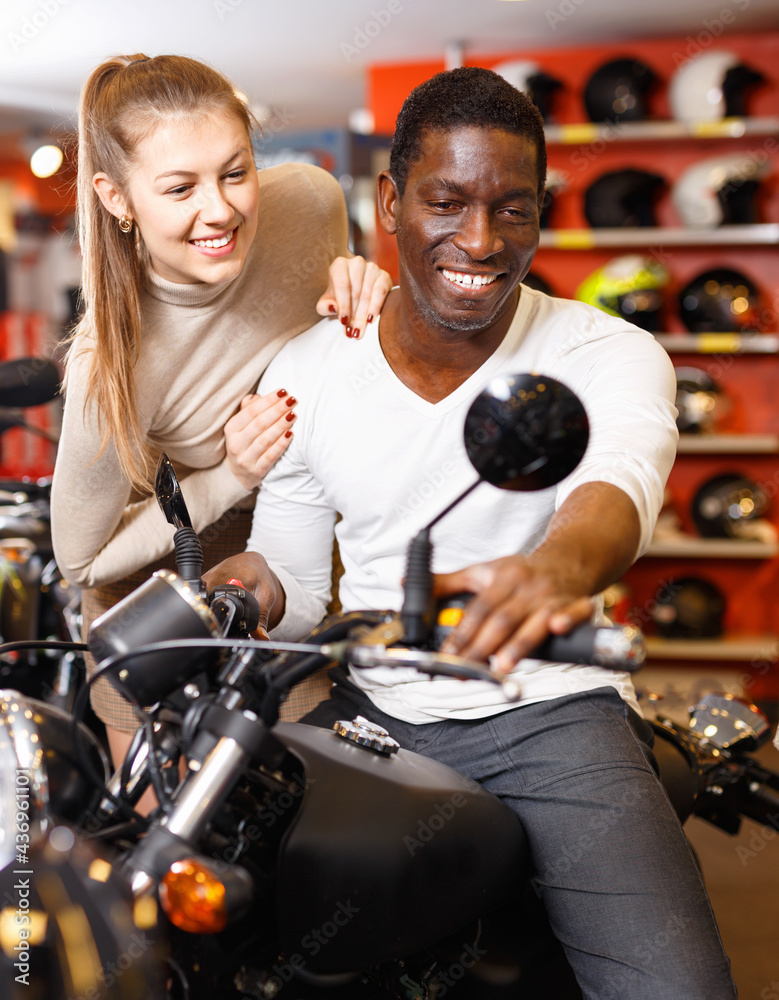 Happy positive smiling young couple choosing and buying new motorcycle in moto salon
