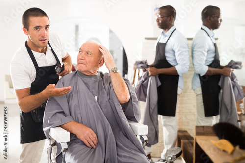 Aged male client expressing dissatisfaction with haircut to perplexed hairdresser at barber shop