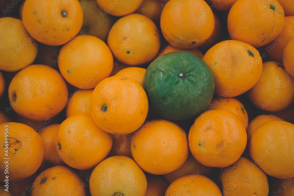 Stack of orange fruit with one green orange placed on top stock orange fruit.