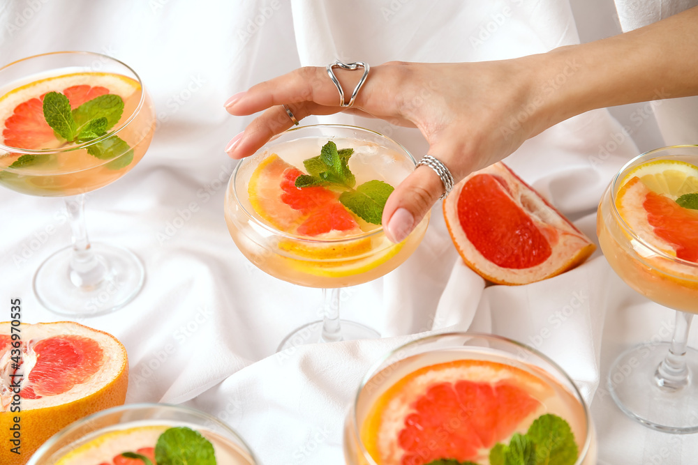 Female hand with glass of tasty grapefruit cocktail on fabric background