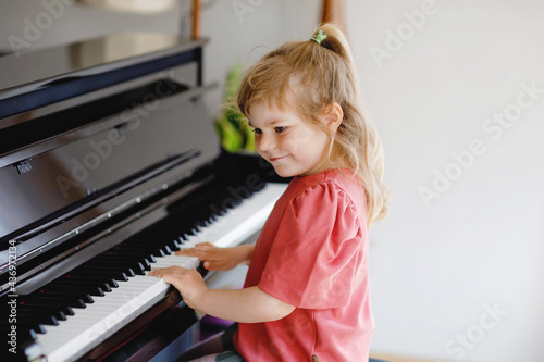 Beautiful little toddler girl playing piano in living room. Cute preschool child having fun with learning to play music instrument. Early musical education for children.