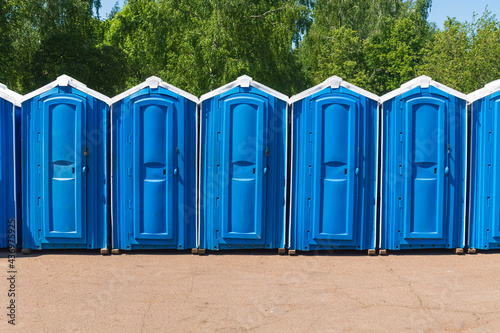 Blue plastic biodegradable toilet stalls line up in an outdoor activity area.
