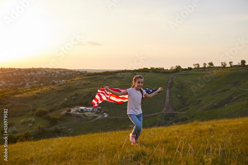 Girl with American flag running through the field at sunset in nature.