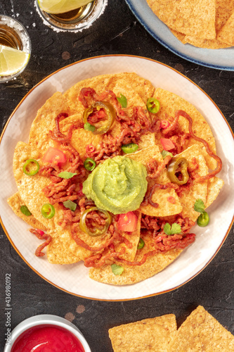 A plate of nachos, Mexican tortilla chips, overhead shot on a black background