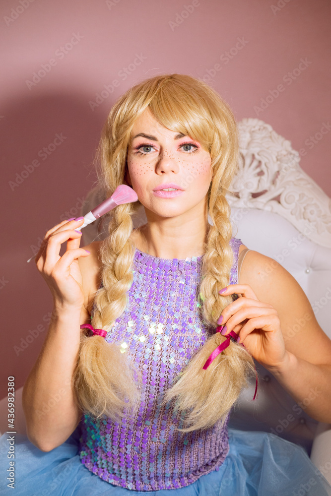 Lady in the doll costume makes makeup, blush. A wig and a beautiful elegant dress for a thematic holiday. Lady in the doll costume makes makeup, blush. A wig and a beautiful elegant dress for a thematic holiday.