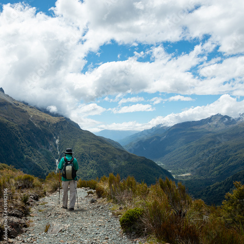 A man hiking on the Key Summit with views of the valleys under the white fluffy clouds, Routeburn Track, South Island. Vertical format