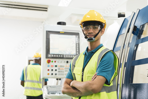 Young Asian male worker in yellow helmet smile with confidence in front of machine in factory production line with copy space.