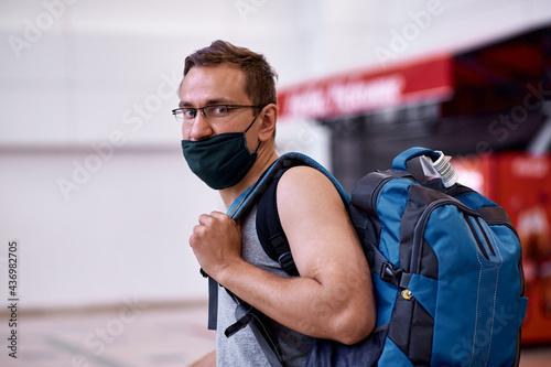 Masked passenger with luggage at the lobby of airport. Tourism during a pandemic of coronavirus. Blurred background. High quality photo