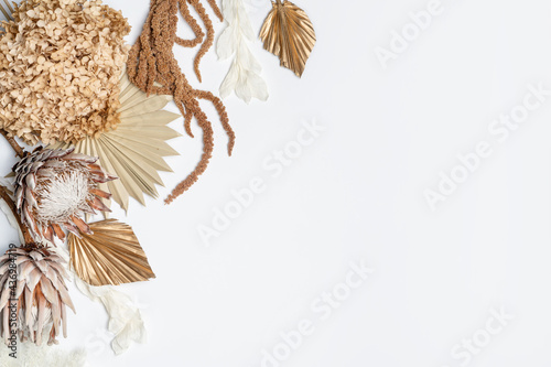 Rustic dried flower arrangement of King Proteas, Hydrangea, Ruscus leaves, Amaranthus and Palm fronds, photographed from above, on a white background. Earthy tones of brown, cream, pink and gold.
