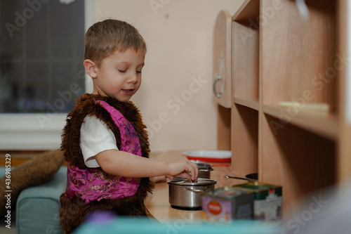 Принти на полотні cute caucasian boy in carnival costume of bear playing with toy kitchen in kindergarden pretending cooking on stove
