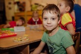 cute caucasian boy sitting at the table in kindergarden smiling. Image with selective focus