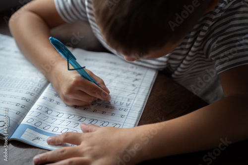 close up top view of boy's  hands writing russian cursive letters in a copybook. Image with selective focus photo
